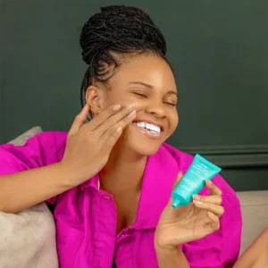A model smiling and holding a product in her hand (Sunscreen) which is an important product to have when exfoliating your skin