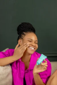 A young woman smiling as she applies something on her face as part of her dsily self care routine