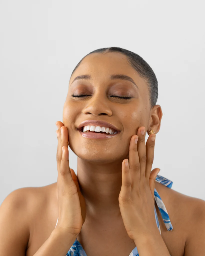 Lady holding smiling and placing her hands on her cheeks showing proper selfcare and positive mental health ideas