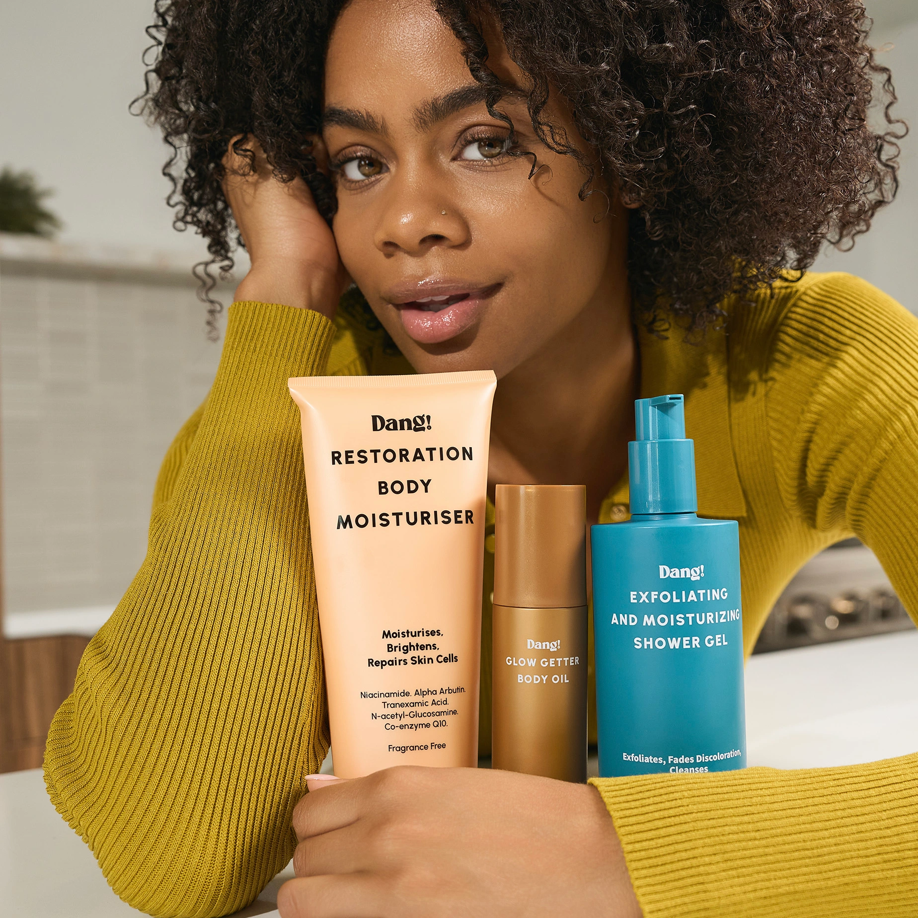 Model holding 3 skincare products in the body glow set for glowing skin