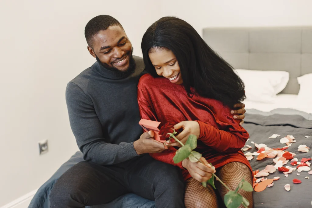 A couple sitting on the bed celebrating Valentine with the man giving his girlfriend a Valentine Gift